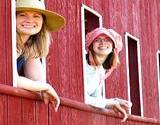 A couple of girls in old fashioned hats smiling out the window of a train at the Kutztown Festival