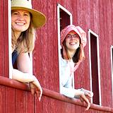 A couple of girls in old fashioned hats smiling out the window of a train at the Kutztown Festival
